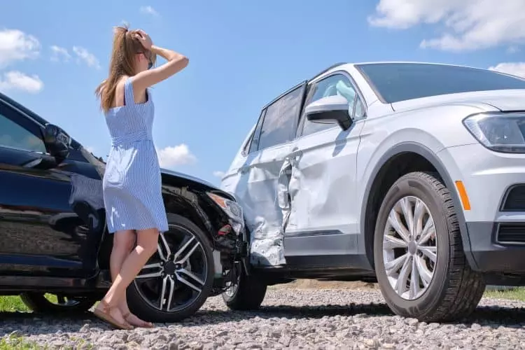 A young sad woman driver standing near her smashed car